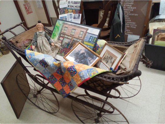 An antique baby carriage with a collection of framed images and a doll inside.